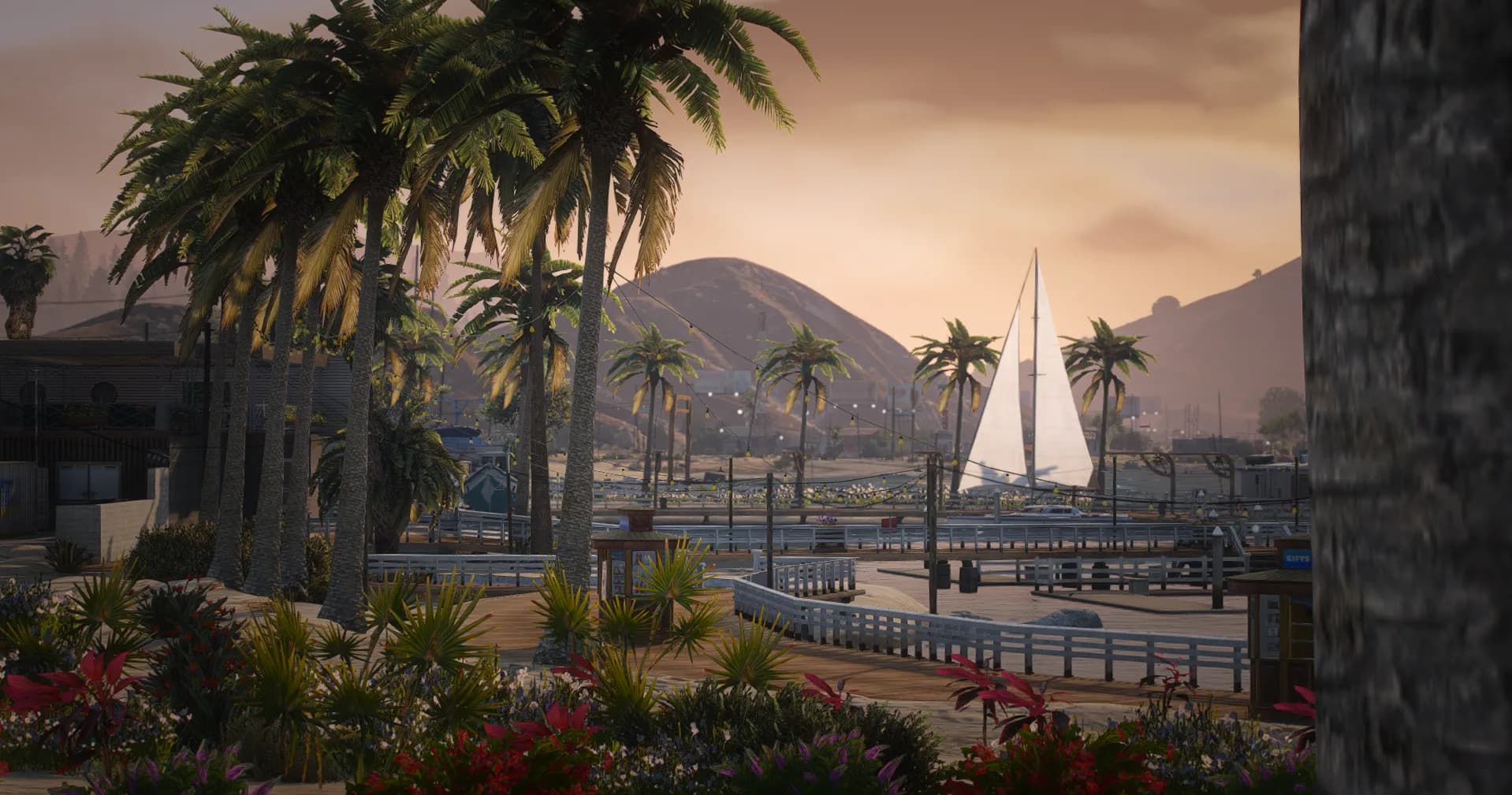Sunset over the marina boardwalk, palm trees and a sailboat docked along the pier